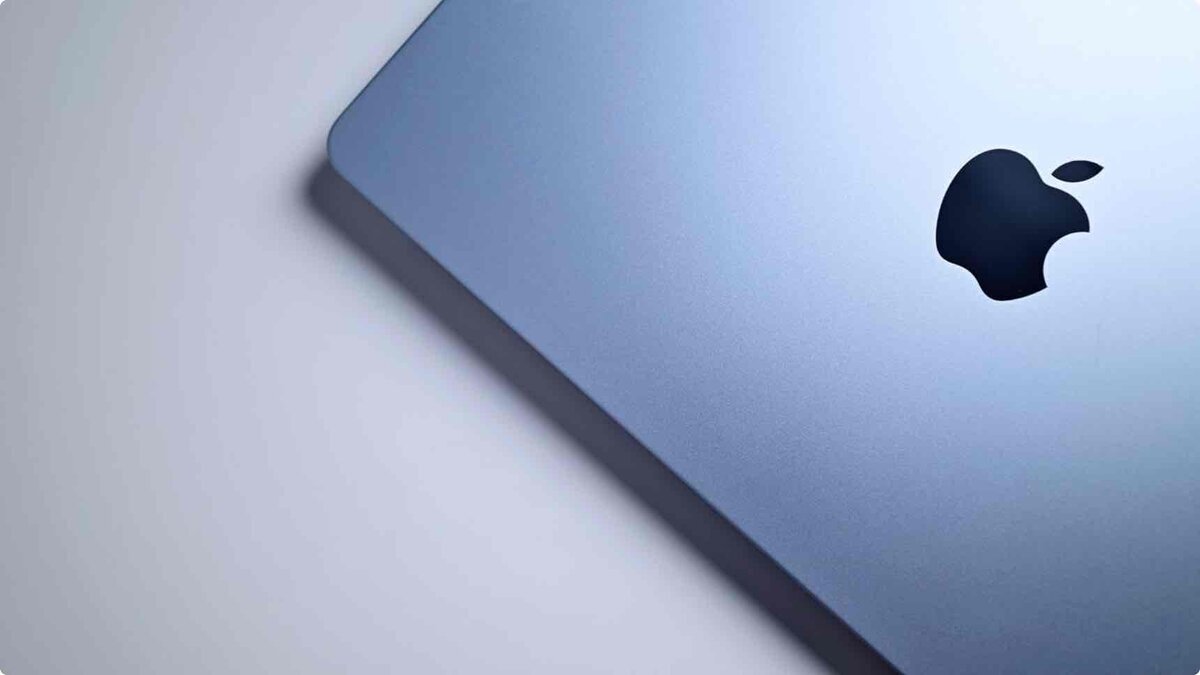 淡いブルーのMacBookの天板を斜め上から俯瞰したクローズアップ。マットな質感のアルミニウムボディに、黒いAppleロゴが中央右寄りに配置されている