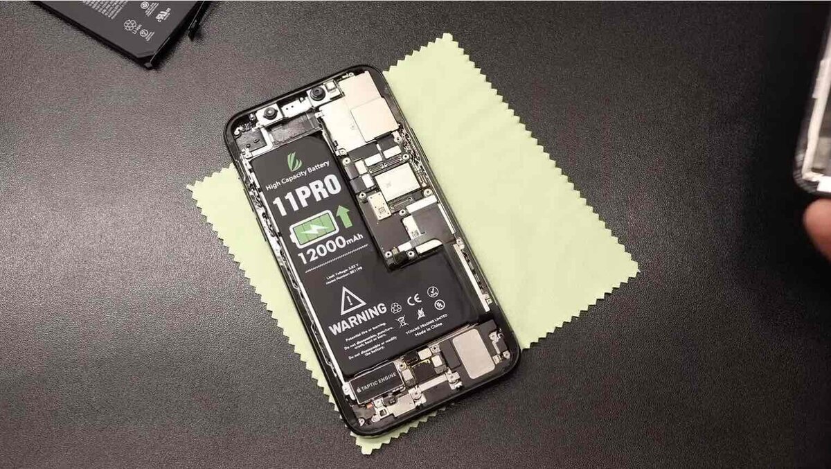 分解されたiPhoneの内部。サードパーティ製と思われる「11PRO」および「12000mAh」と印字された大容量バッテリーが装着されており、クリーニングクロスの上の作業台に置かれている様子
