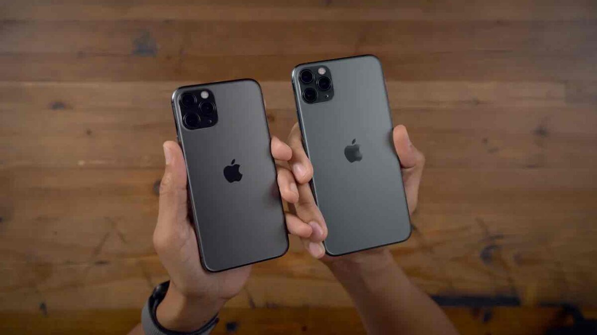 木目の背景の前で、トリプルカメラを搭載した2台のiPhone Proモデルを手に持って比較している様子
