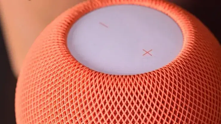 オレンジ色のHomePod miniを真上から見たところ。メッシュ生地の上面に音量のプラスとマイナスのマークが見える