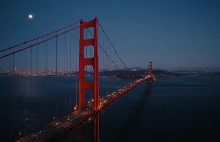 満月とサンフランシスコの夜景を背景に、ライトアップされて赤く浮かび上がる夜のゴールデンゲートブリッジ