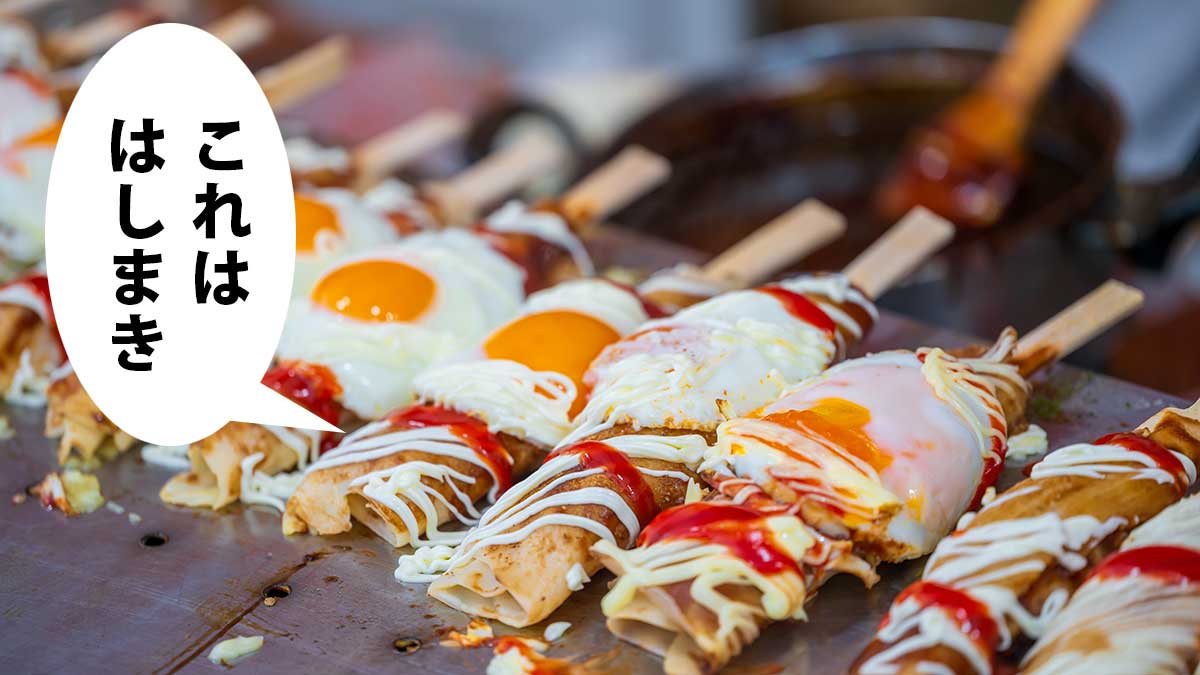 お好み焼きのようなものを箸に巻き付けて目玉焼きを乗せたはしまきの屋台。吹き出しに「これははしまき」
