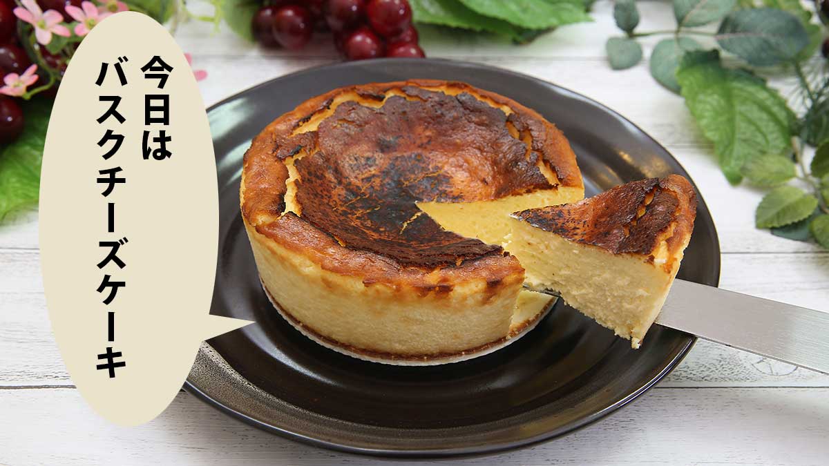 バスクチーズケーキを１切れ切り分けたところ。背後にはツタやぶどう、カタバミの花が飾ってある。吹き出しに「今日はバスクチーズケーキ」