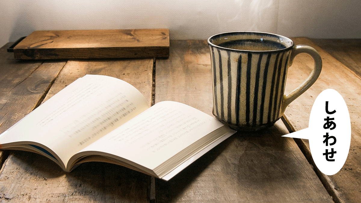 古さが落ち着く木の机に開いた文庫本とコーヒーを入れたマグカップ。吹き出しに「しあわせ」