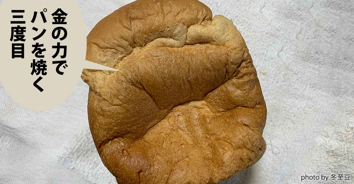 まるごとの食パンが布巾の上に乗っている。吹き出しに「金の力で パンを焼く 三度目」