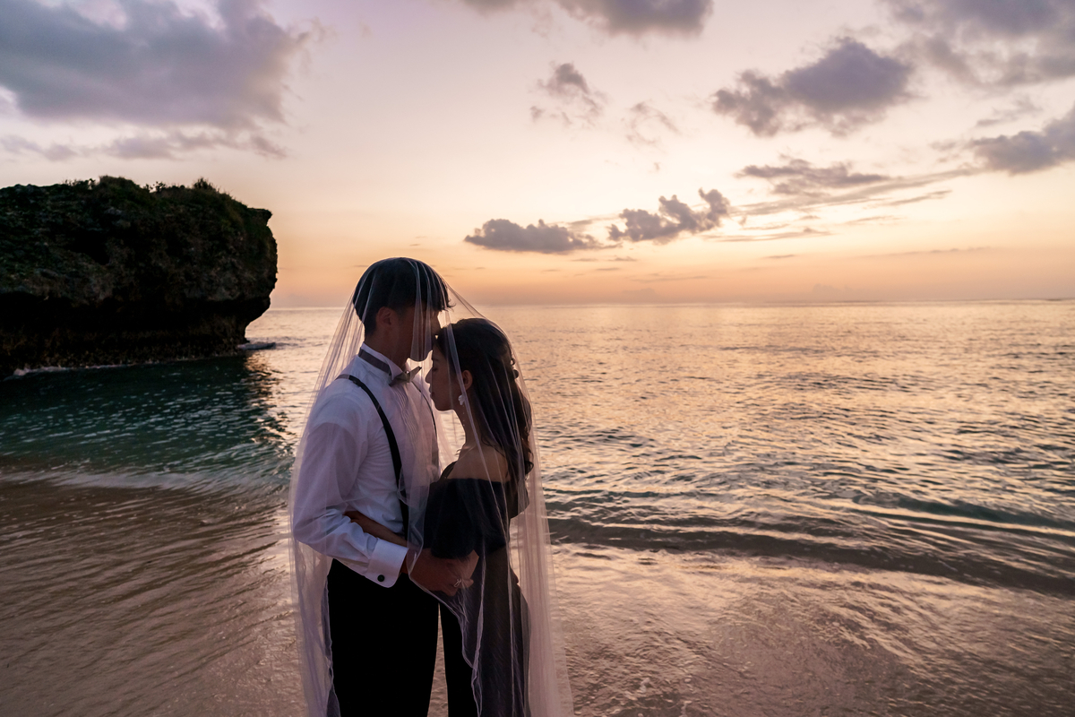 沖縄の隠れ家ビーチでサンセットの柔らかい光に包まれた新郎新婦のウェディングフォト