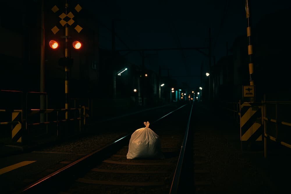  夜の踏切と線路の上にポツンと置かれたゴミ袋