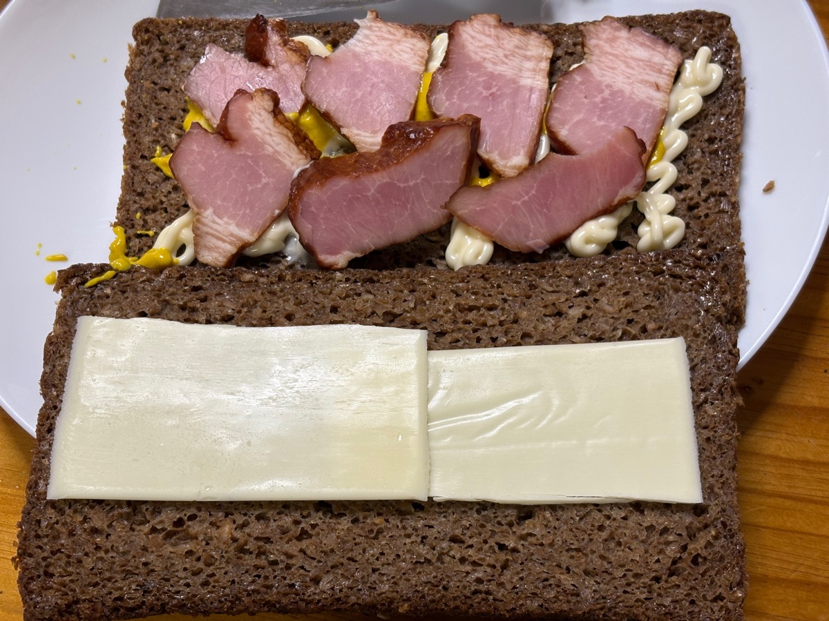 "ドイツパンで作ったベーコンとチーズのみのシンプルなサンドイッチを作っている途中の写真。"