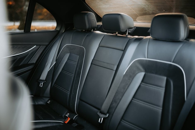 車の後部座席のヘッドレストに固定された黒い樹脂製の折りたたみテーブル。テーブル面にはタブレットスタンドとカップホルダーが見える。