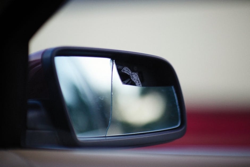 駐車中の車の運転席側サイドミラーが割れ、その横に広げられたタブレット画面には修理費用と複数の対応策が表示されている。