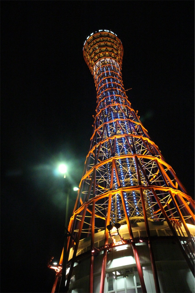 夜、真下から見上げた神戸ポートタワー。赤い金属の骨組みがライトに照らされている。