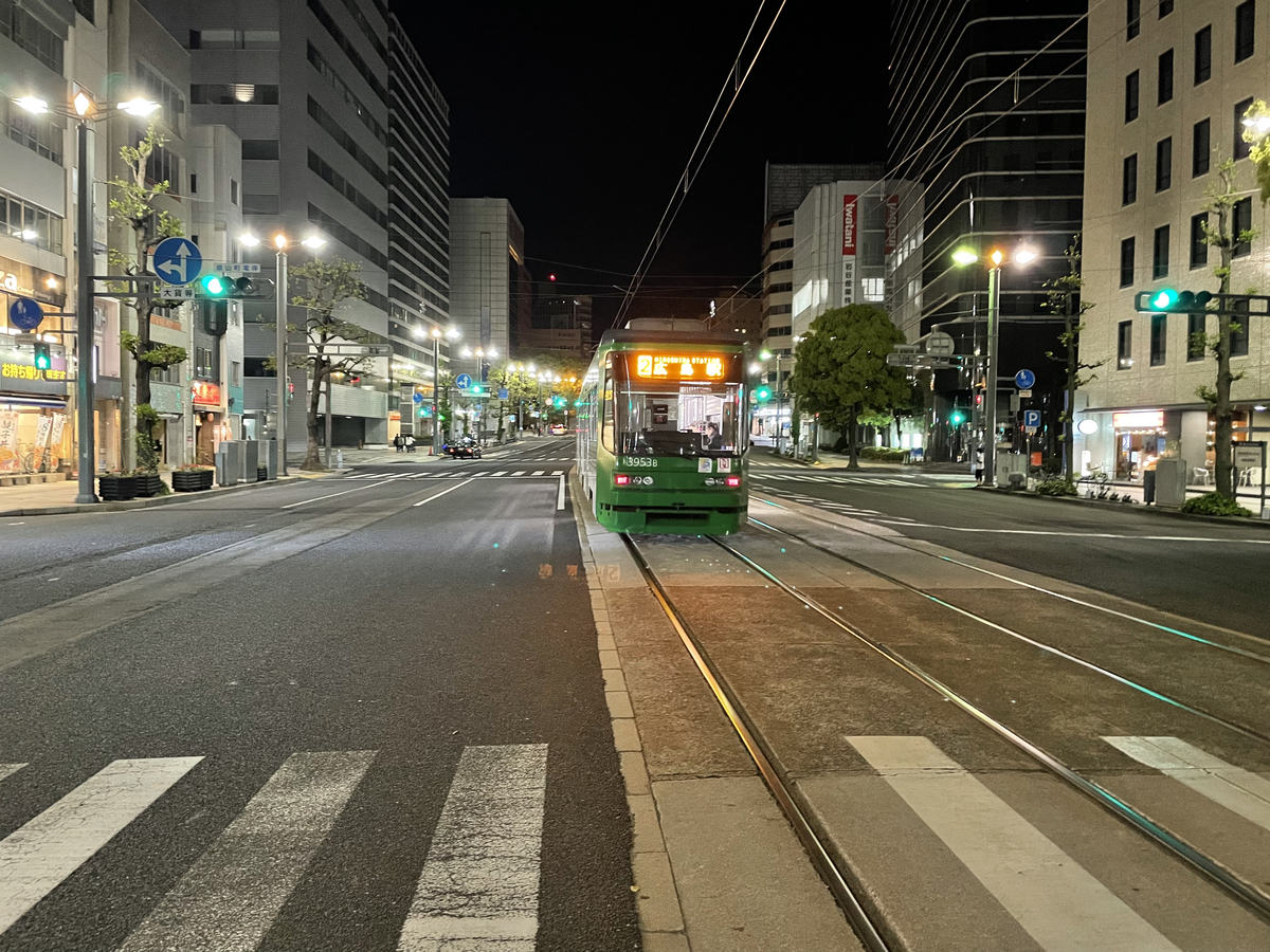 夜の広島の市街地を向こうへ走っていく広電の写真。LED行先表示に「広島駅」、道にはタクシーが1台。