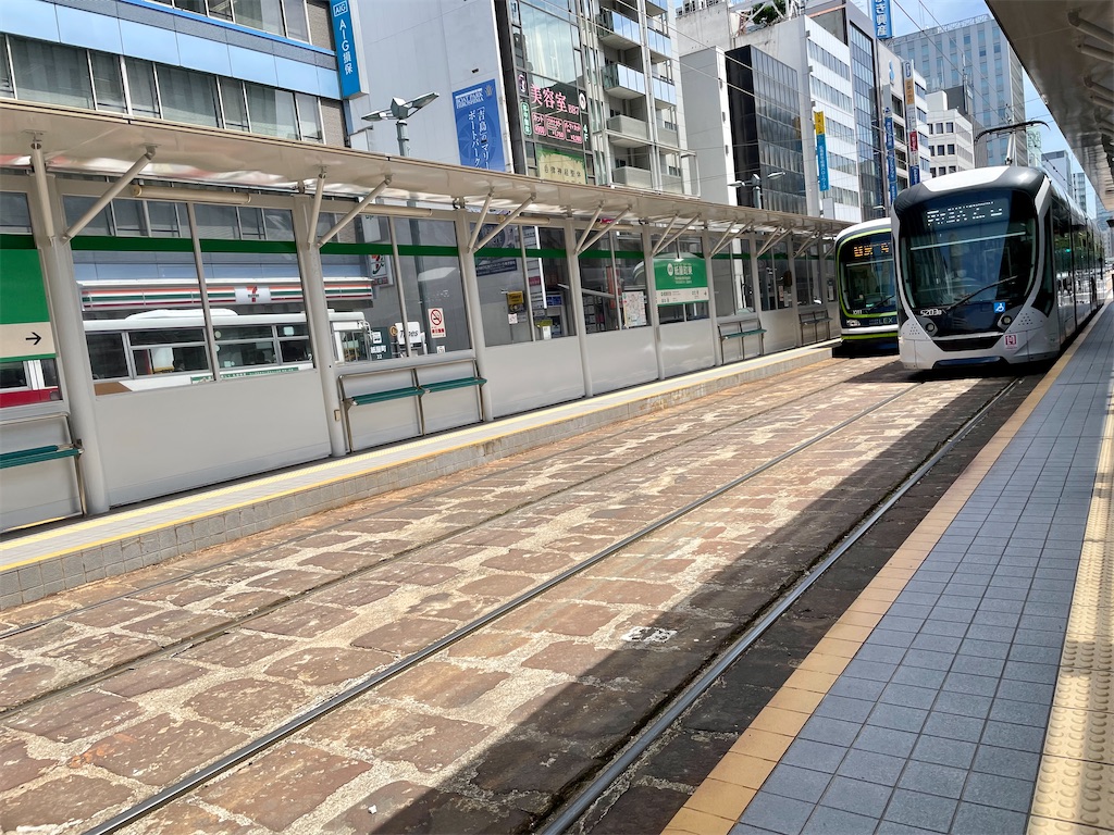紙屋町東駅の写真。軌道敷が年季の入った石造で、赤い。電停には新しい壁と屋根があり、超低床車両が向こうとこちらの線路に１台ずついる。