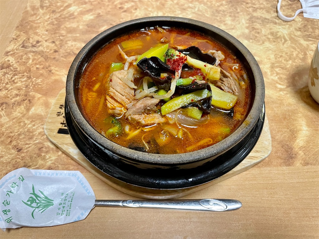 石鍋に入ったユッケジャンクッパの写真。赤いスープに、細長いすじすじした牛肉、キュウリ、キクラゲ、ブロッコリー、玉ねぎなどがのっている。