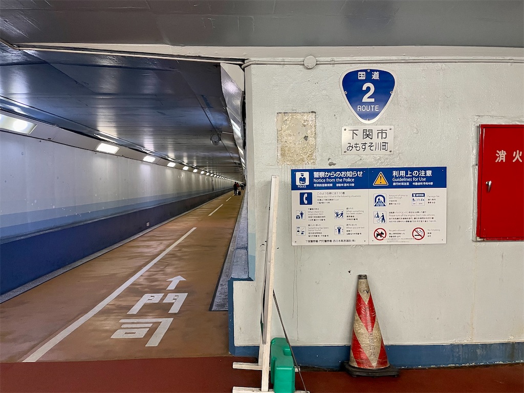 関門トンネル、下関側の写真。国道2号線の三角の表示、下関市みもすそ川町。左にトンネル、地面に「↑門司」と書かれている。トンネルは真ん中に点線が引かれ、右側通行になっている。