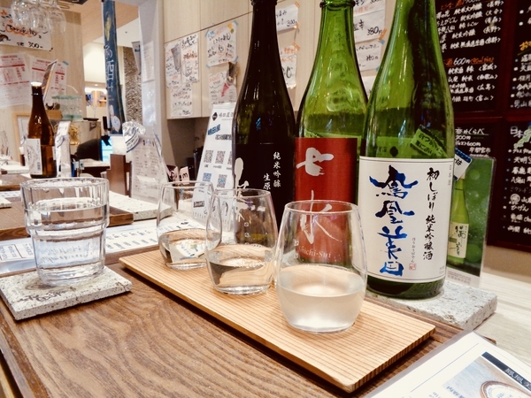 日本酒の四合瓶が並んでいて、その前に角打ち用の器が三つ並んでいる