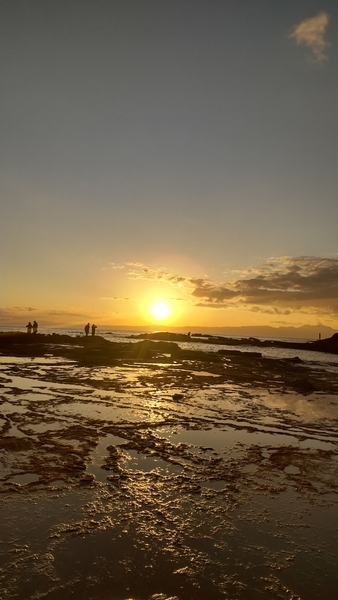 岩場の向こうに広がる海、その向こうで日がかげっていく