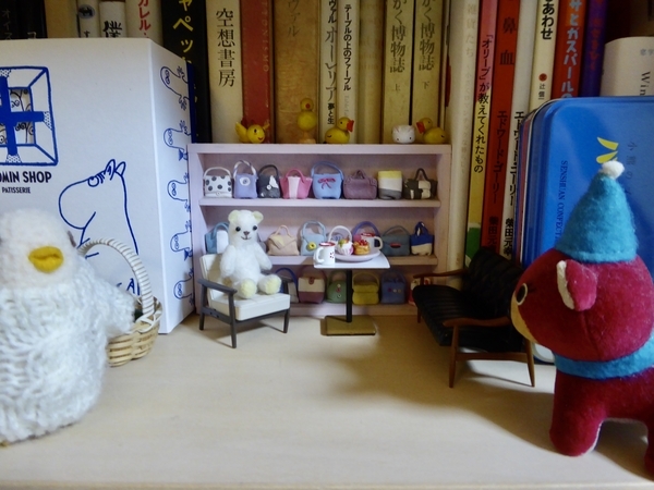 本棚の一隅にミニチュアの家具が置いてある。そこに小さなぬいぐるみが入ってきたところを撮った写真。