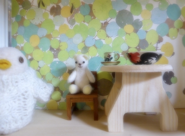 小さなくまのぬいぐるみの写真。手前にちいさな鳥のぬいぐるみがいて、くまは木の椅子に座っている。