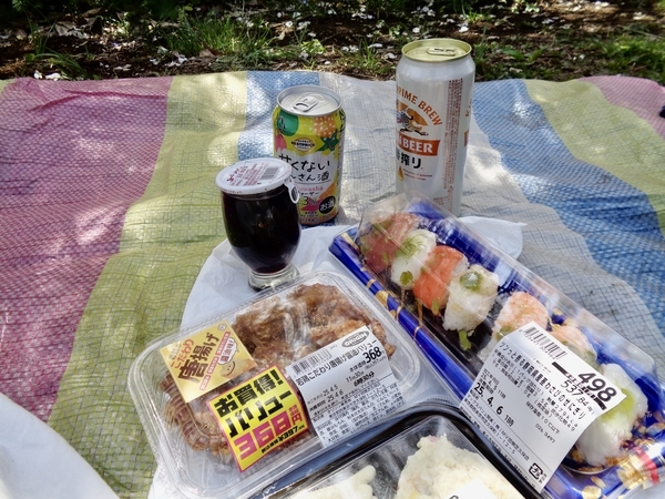 ピクニックランチの写真。缶ビールや赤ワイン、お寿司などがピクニックシートの上に置かれている。