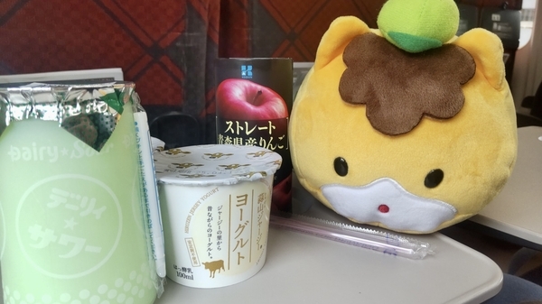 新幹線の席の写真。飲み物やヨーグルトといっしょにぐんまちゃんのぬいぐるみがテーブルにいる。