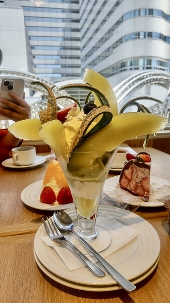 メロンパフェの写真。奥にケーキがふたつ映り込んでいる。