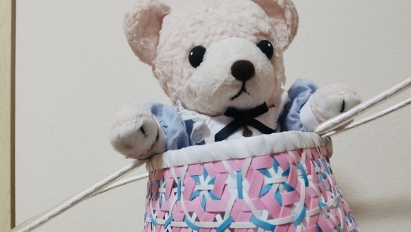 ぬいぐるみの写真。エプロンドレスをきた熊のぬいぐるみがかごに入って遊んでいる。