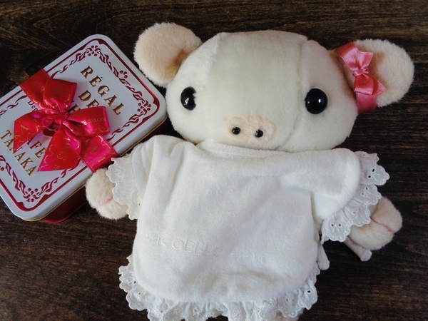 クッキー缶とぬいぐるみの写真。ぬいぐるみは子豚で、リボンをしている。白とピンクの色使いが重なっている。