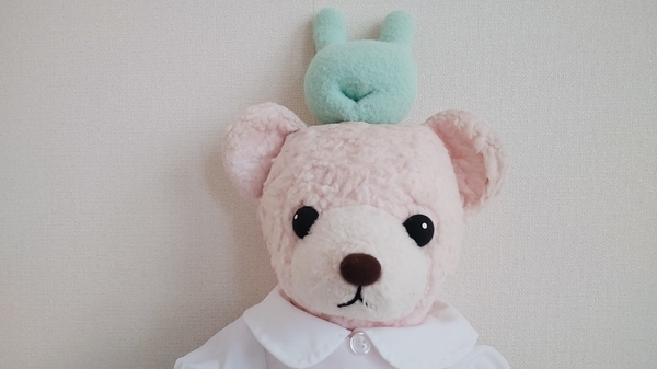 ぬいぐるみの写真。丸えりの服を着たくまが頭に「ふかふか手枕」というストレッチボールをのせて遊んでいる。