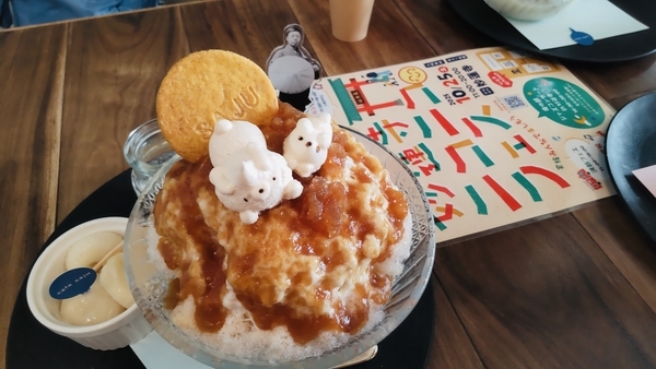 かき氷の写真。みたらしシロップがかかっていて、上にくまのメレンゲと月をかたどったぱりっとしたお菓子がのっている。中にはあずき。ミルクシロップと白玉が添えてある。正岡子規のアクリルスタンドがそれを見ている。