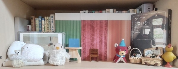 本棚の写真。本棚の一隅に小さなぬいぐるみや木彫りのおもちゃが暮らしている。