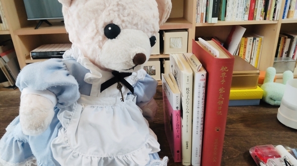 本とぬいぐるみの写真。四冊の本とエプロンドレスを着たくま。