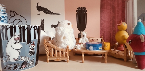 小さなぬいぐるみや木彫りのおもちゃの暮らしぶりを撮った写真。テーブルにクッキーとコーヒーカップが出ている。手前に人間用マグカップがある。