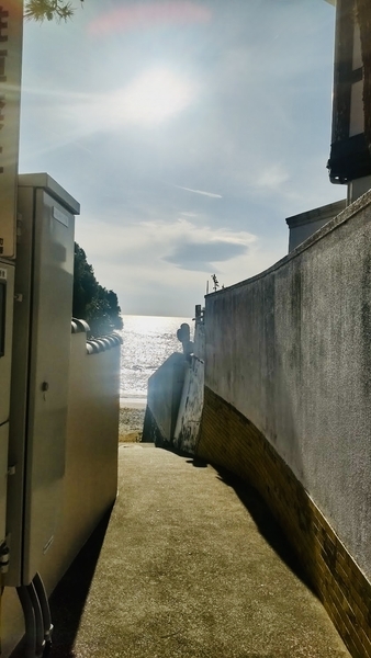 白い壁に挟まれた路地の写真。向こう側に海が見える。