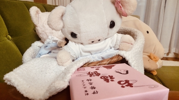 ぬいぐるみの写真。耳にリボンをつけたこぶたがピンクの紙につつまれた箱を見ている。