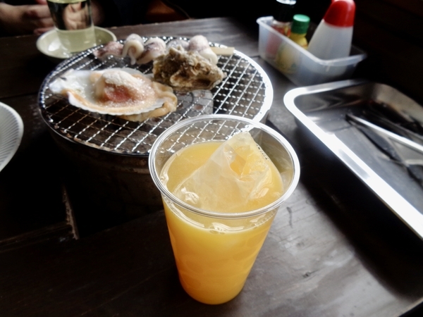 居酒屋店内の写真。テーブル備え付けの七輪でで牡蠣、ホタテ、イカを焼いている。