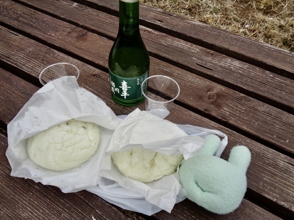 お昼ごはんの写真。日本酒「喜平」とにくまんがベンチの上に並んでいる。