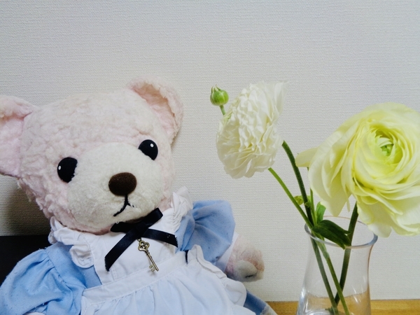 ぬいぐるみの写真。エプロンドレスを着たくまが花を見ている。