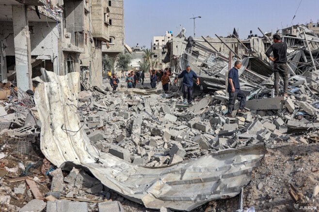 １８日、パレスチナ自治区ガザ北部のガザ市で、イスラエル軍に破壊された建物のがれきの中を歩く人々。