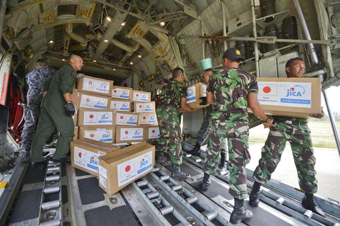 　パルの空港に到着した航空自衛隊のＣ１３０輸送機から救援物資を運び出す隊員とインドネシア軍の関係者ら＝６日、インドネシア・スラウェシ島（共同）