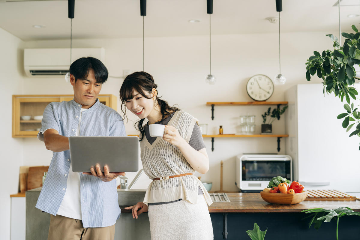 キッチン前でパソコンを使う夫婦のイメージ