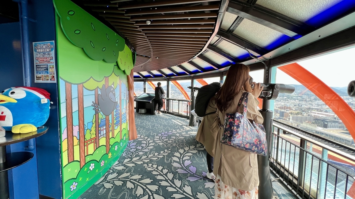望遠鏡で京都市街を眺める来場者とカラフルな壁面アートが見える展望室内