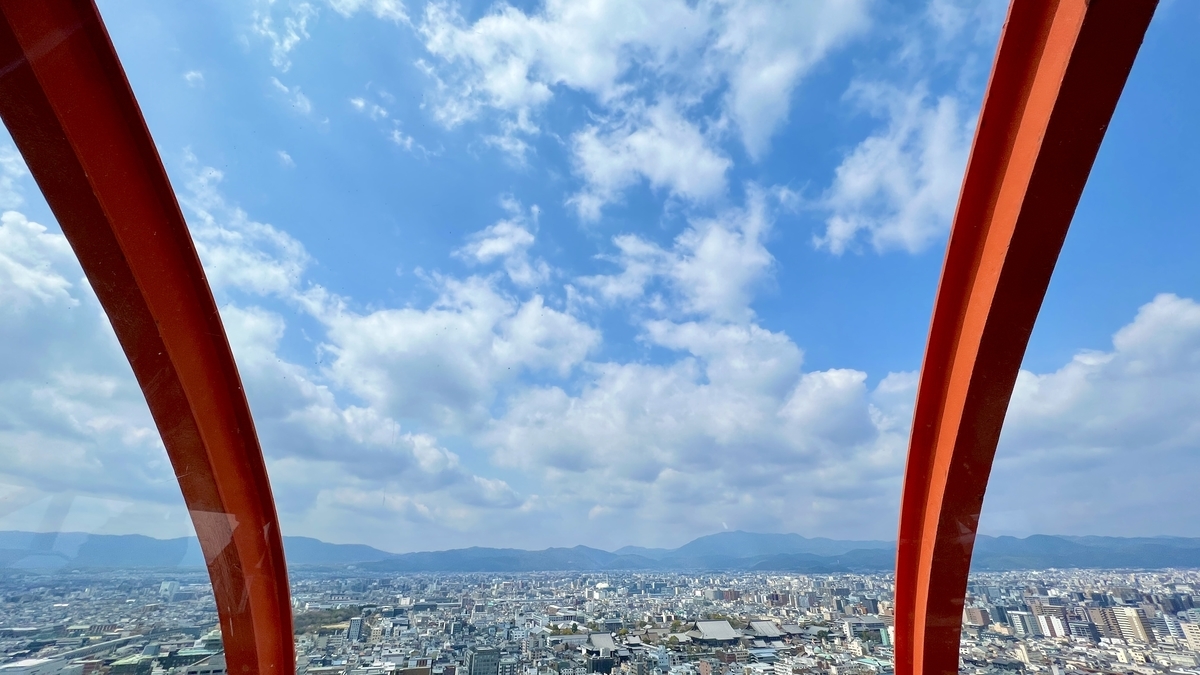 オレンジの支柱がフレームになった展望室の窓から見る青空と京都市街