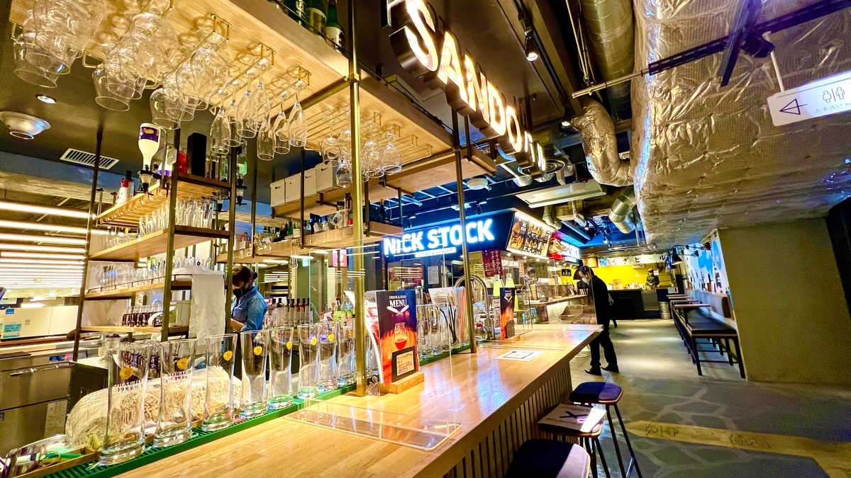 バーカウンターとNICK STOCKの看板が見えるダクトむき出しのモダンなフードホール