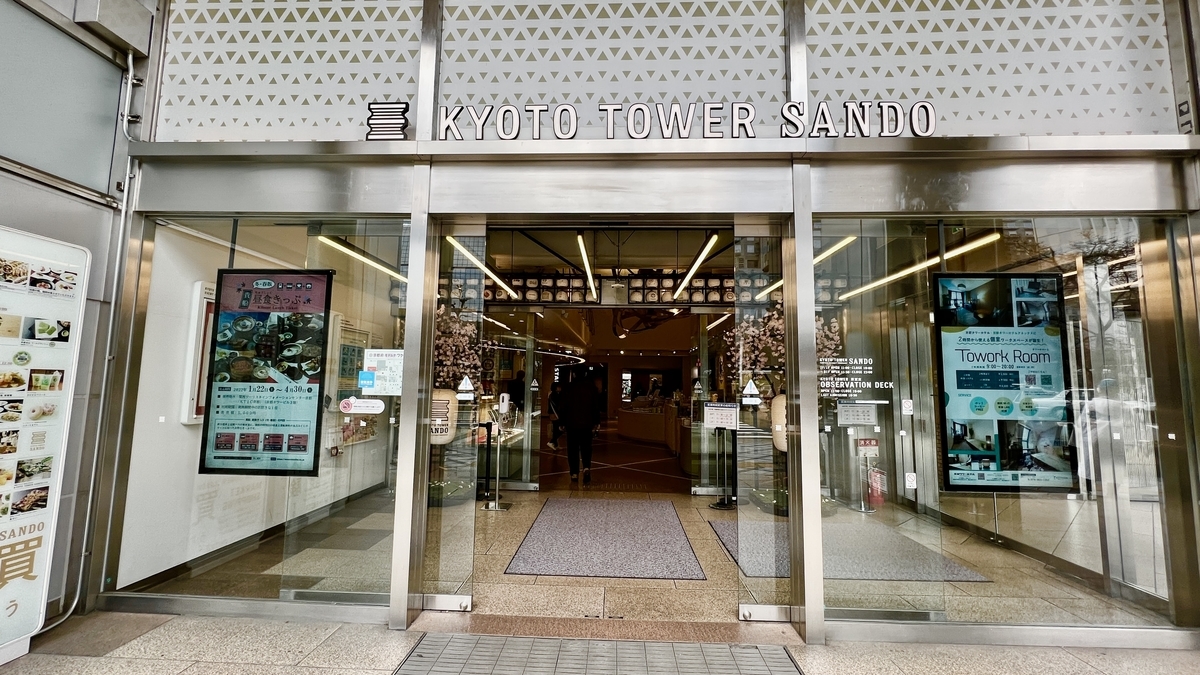 KYOTO TOWER SANDO の看板が掲げられた京都タワービル東南角入口のガラス扉