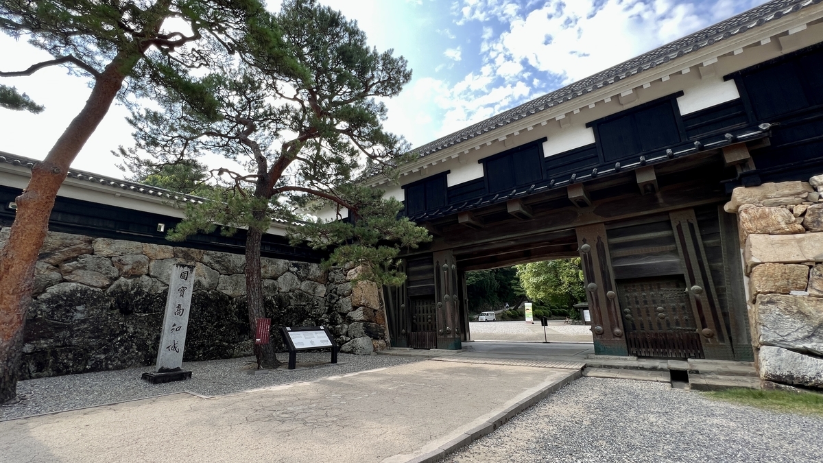 松の木に囲まれた追手門。門をくぐる視点で見た石畳の道