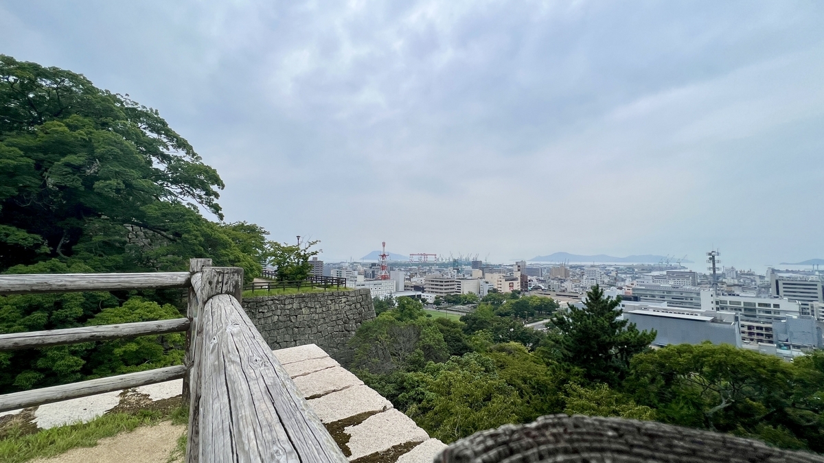丸亀市内と瀬戸内の景観が調和した遠望。木製柵と石垣の曲線が印象的