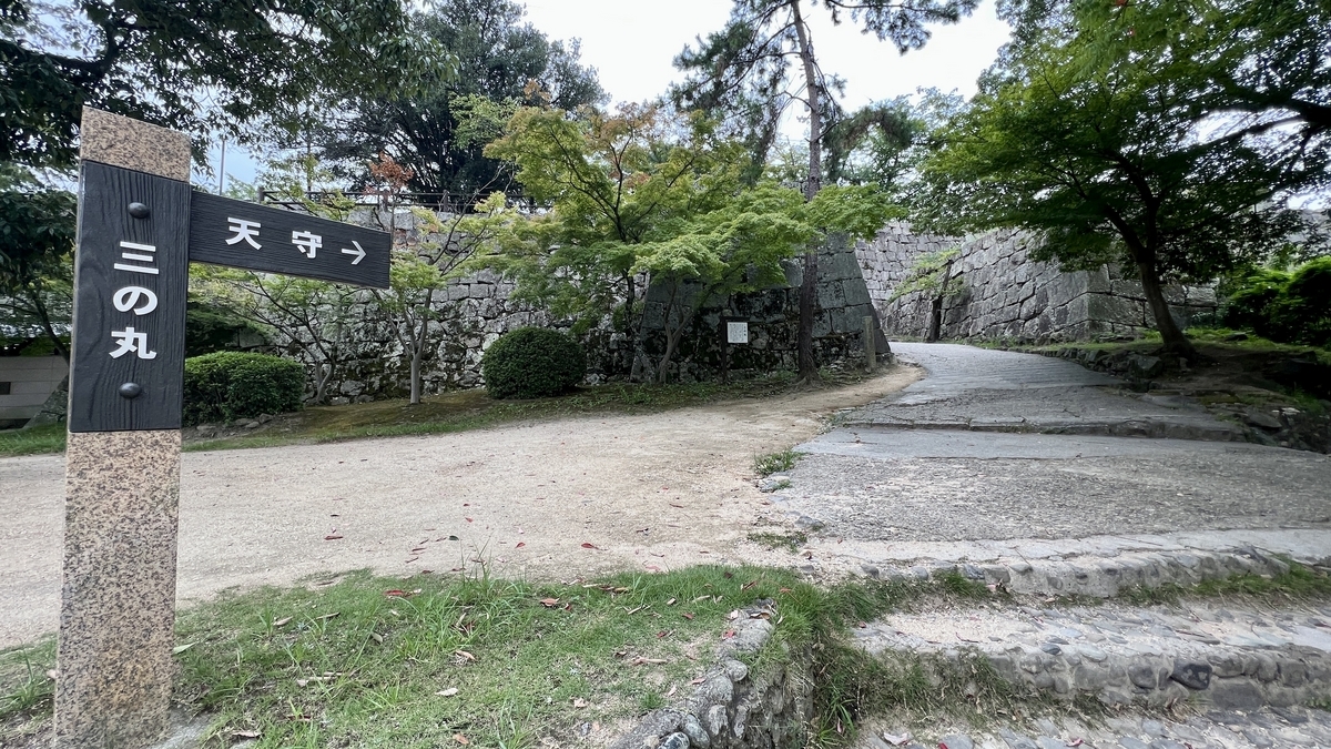 天守へ続く道の分岐点に立つ道標と石垣。「天守」方向を指す案内表示