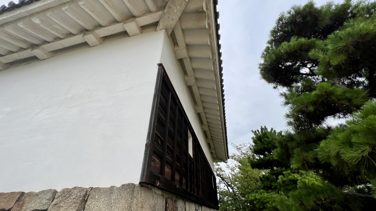 天守の白壁と屋根の軒裏。建築の細部と松の木の緑が調和する