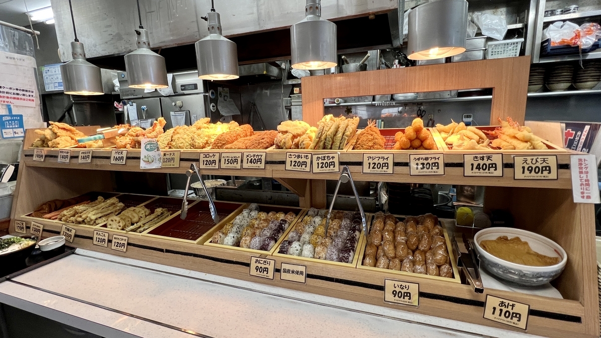 天ぷらやおにぎりなど種類豊富に並ぶめりけんやのトッピングコーナー